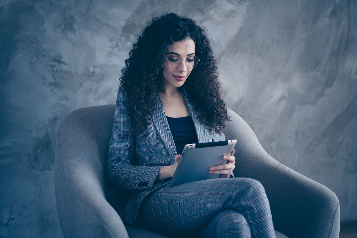 商务女性一头波浪形头发的经理女孩坐在椅子上阅读平板电脑隔离灰色背景的照片西装平板电脑使用