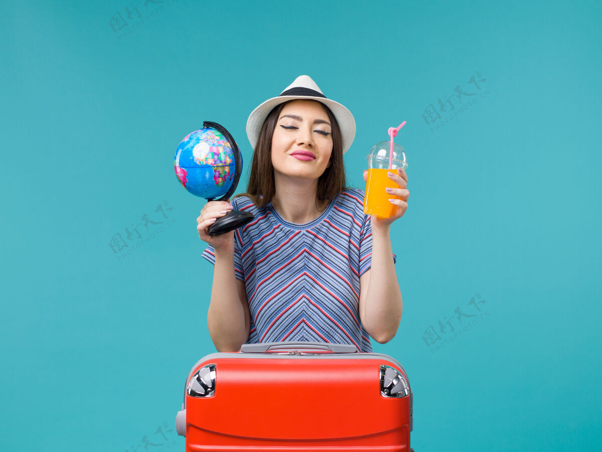 举行前景度假中的女人拿着果汁和地球仪在蓝色的背景海上航行暑假人微笑旅程