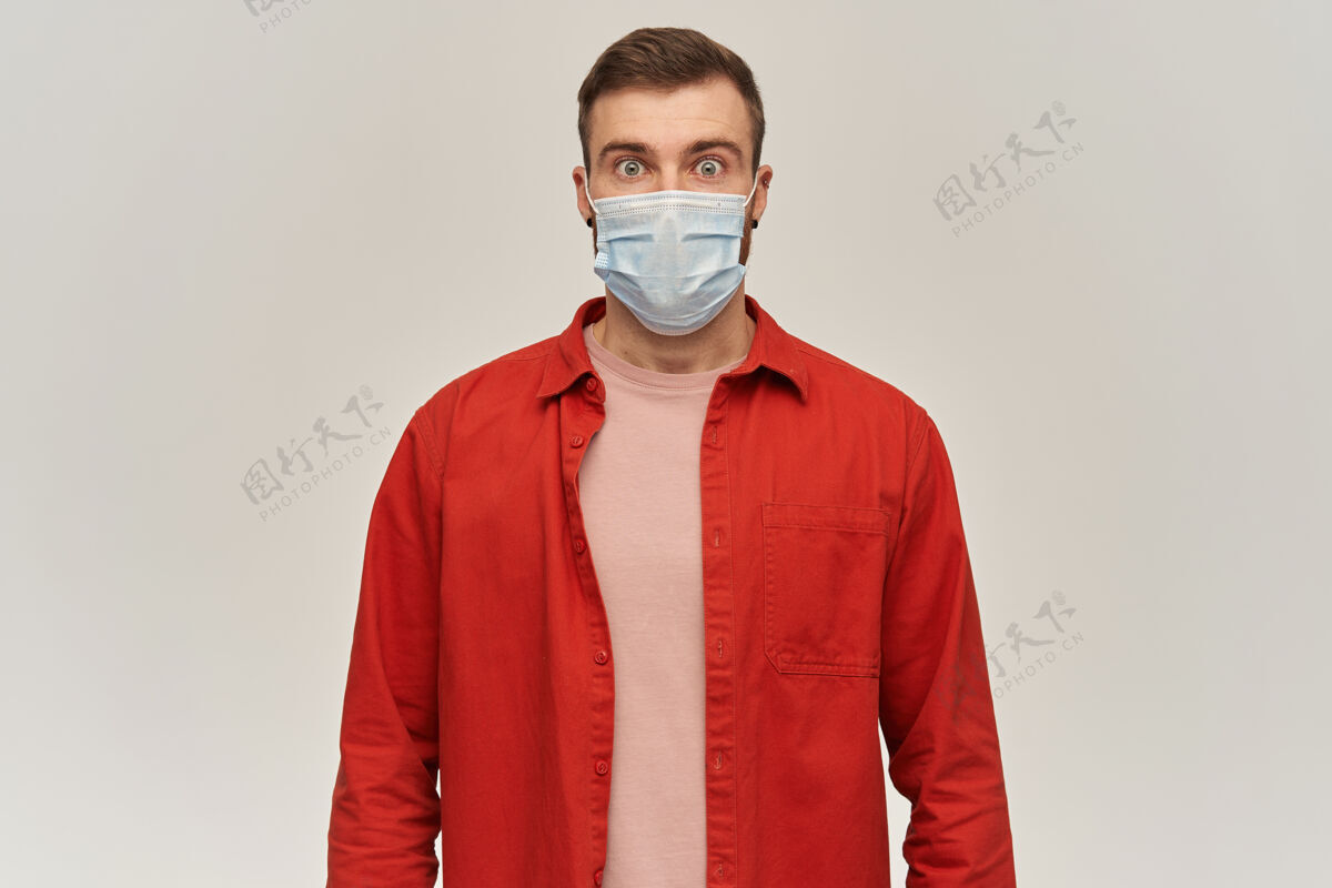 学生那个身穿红衫 脸上戴着防冠状病毒口罩 满脸胡须的年轻人站在白色的墙壁上 望着前方 焦急地惊呆了健康衬衫成人