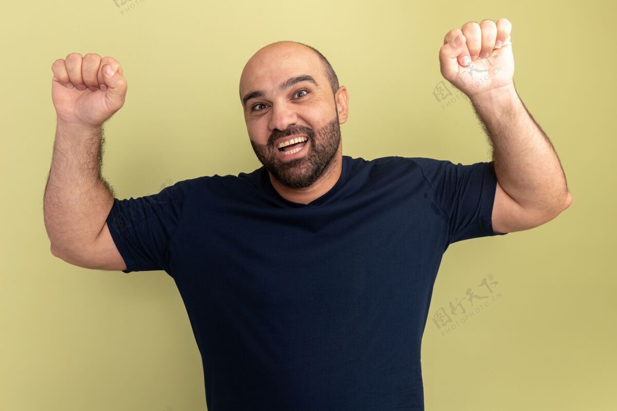 兴奋胡子男人穿着黑色t恤疯狂的快乐和兴奋尖叫握紧拳头庆祝他的成功站在绿色的墙壁表情握紧高兴