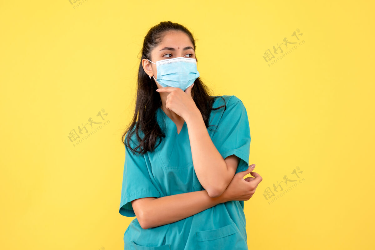 微笑正面图身着制服的美丽女医生把手放在黄色背景上的下巴上人物制服氧气面罩