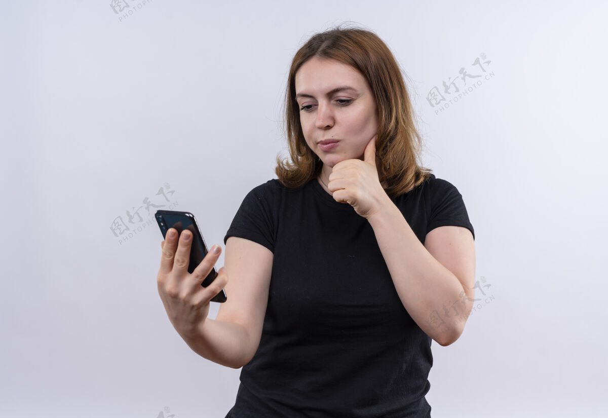 手机体贴的年轻休闲女子拿着手机 把手放在下巴下面 隔着一堵白色的墙 留着复印空间电话下巴女孩