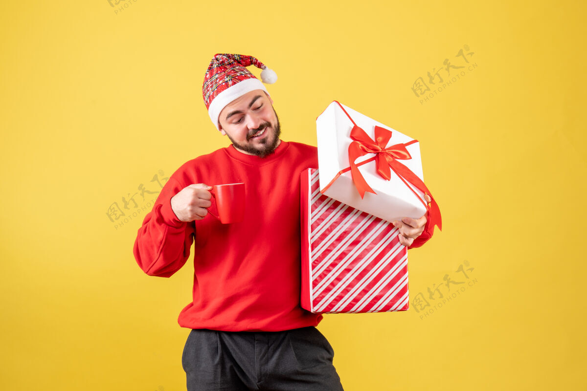 微笑前视图年轻男性 圣诞礼物和黄色背景上的一杯茶礼物背景帽子
