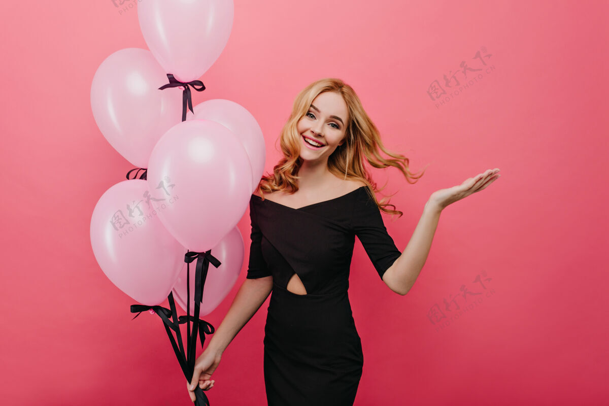 表情可爱的欧洲女孩享受与粉红色气球合影令人惊叹的优雅的女模特在她的生日跳舞卷发明亮室内