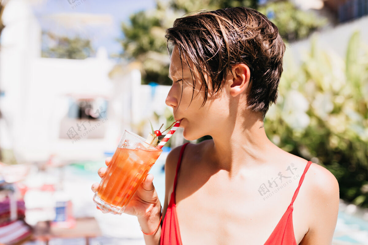 成人一个留着时髦发型的无忧无虑的女孩在度假胜地喝着水果鸡尾酒欧洲泳装快乐