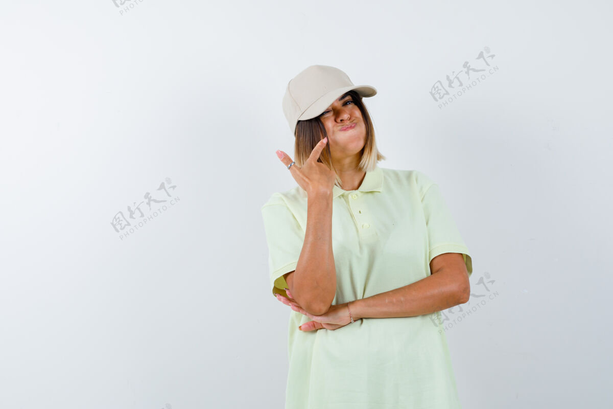 肖像年轻女士指着吹了脸颊在t恤衫 帽子 看起来很有趣前视图黑发前面皮肤护理