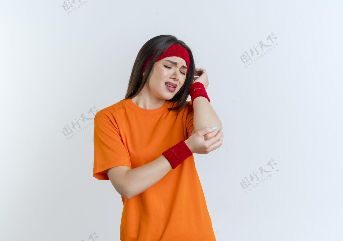 成人疼痛的年轻运动女性戴着头带和腕带手握手肘孤立地看着女人年轻运动