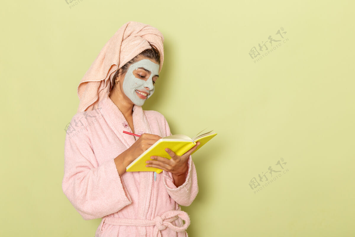 洗澡正面图穿着粉红色浴袍的年轻女性在绿色表面写下笔记书写自我照顾年轻女性