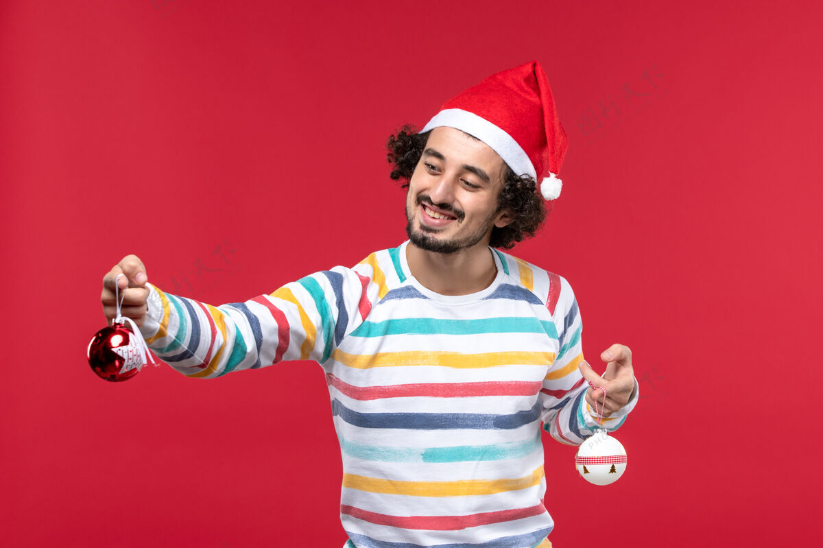 快乐正面图：年轻人拿着圣诞树玩具站在红墙上 新年 节日 红色的人类漂亮举行肖像