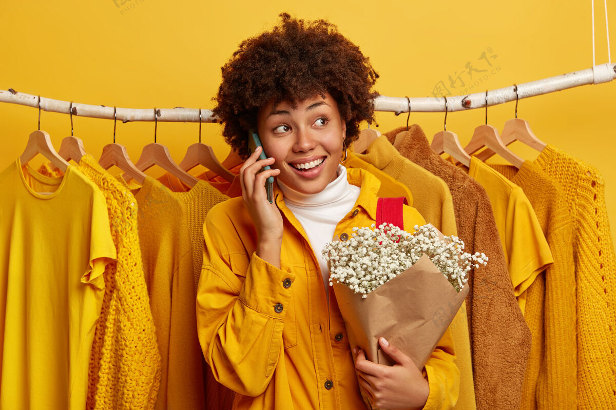 衣服快乐的卷发女人转身离开 通过手机打电话 分享购物日后的印象 摆出一束鲜花短信电子电话