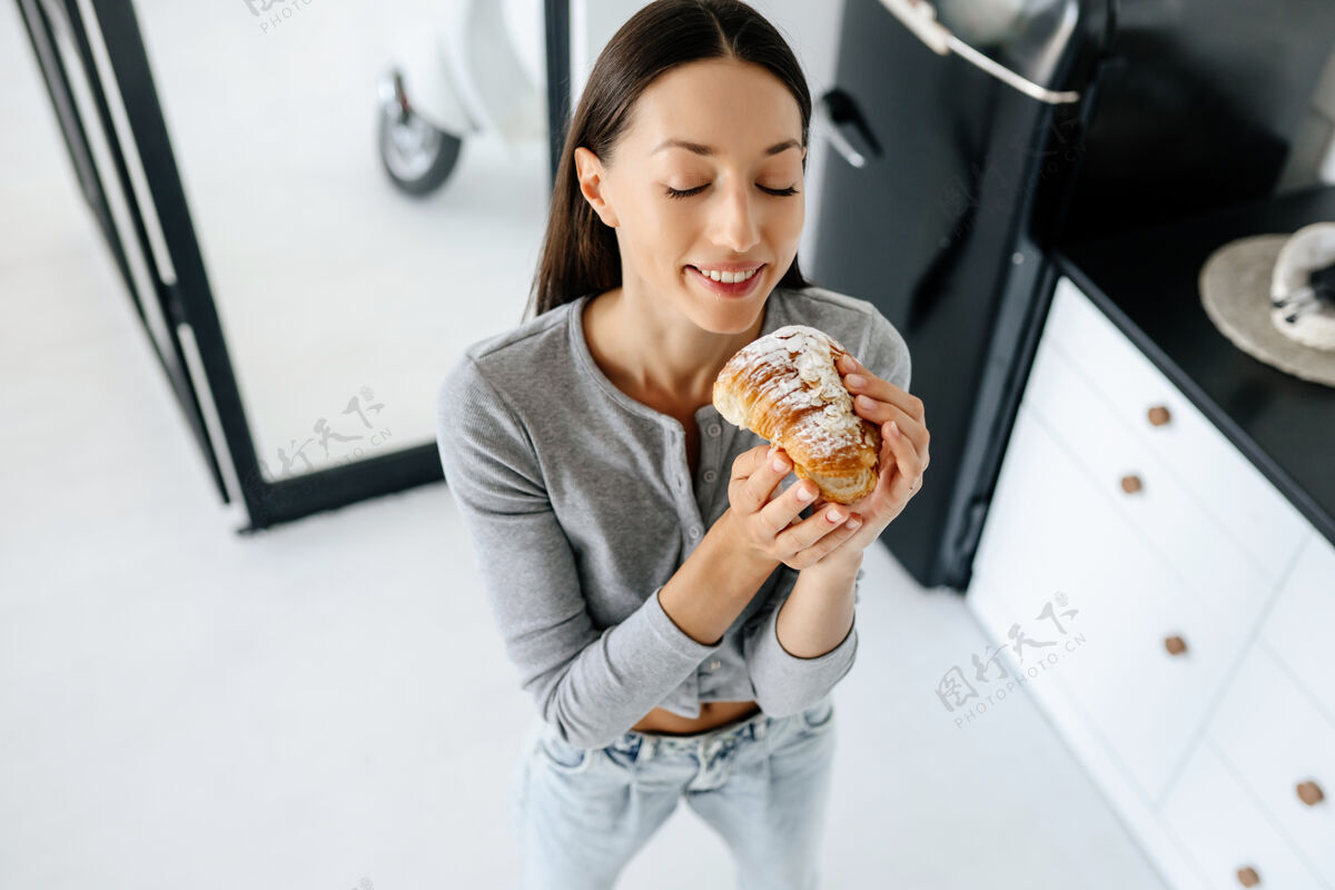脸喜洋洋的女人在家吃美味的羊角面包的画像饥饿美味羊角面包