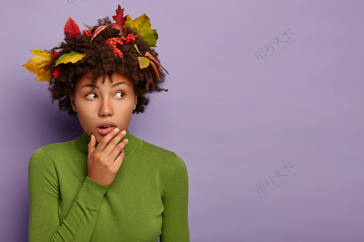 下巴摄影棚拍摄的受惊吓的美国黑人妇女抚摸着下巴往旁边看 穿着随意 留着秋叶的卷发 隔离在紫色的墙上天哪年轻随意