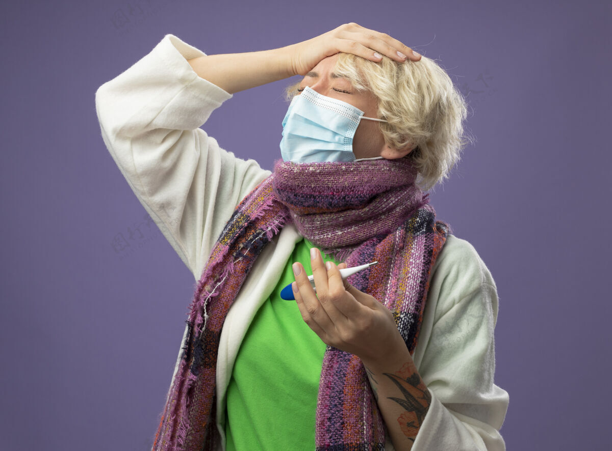 触摸生病的不健康的女人 短头发 戴着暖和的围巾 戴着面罩 拿着温度计 闭着眼睛 在紫色的背景上站着保护封闭温暖