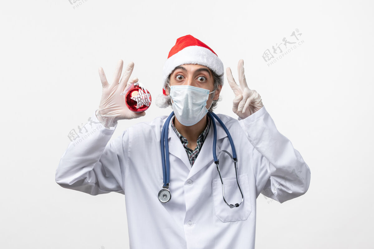 医生正面图戴面具的男医生带着玩具在白墙上健康病毒共舞新年视图男人制服