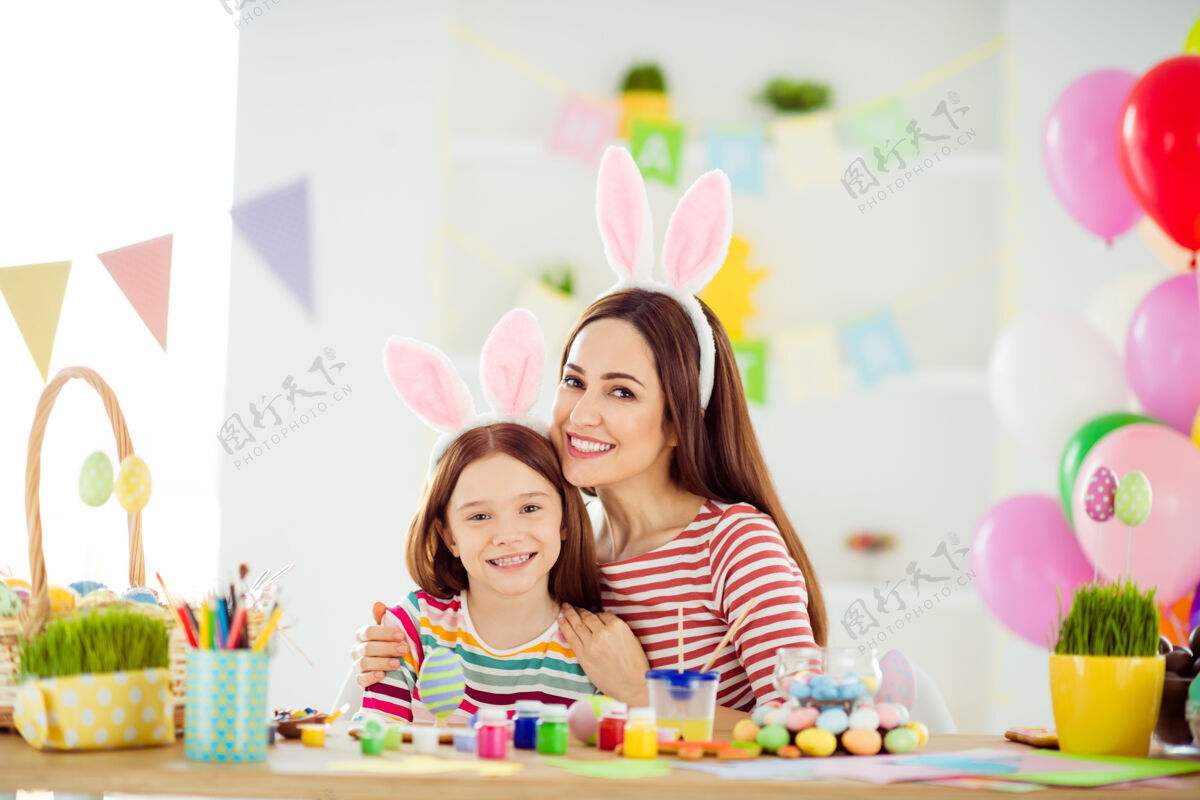 微笑两个漂亮可爱开朗开朗活泼的小女孩的特写肖像戴着兔子耳朵的小女儿在白色灯光的房子里做手工拥抱工艺孩子舞会