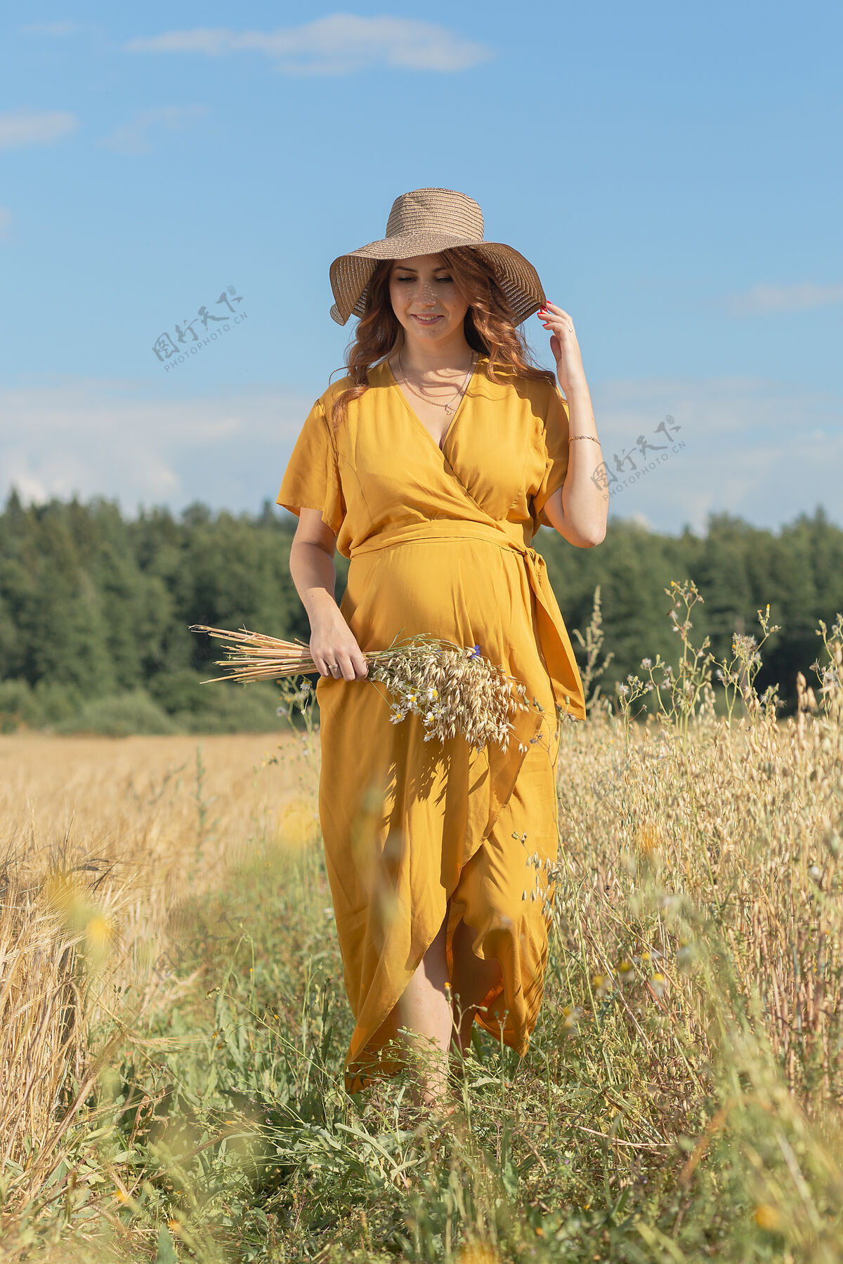 父母在一个阳光明媚的夏日 一位年轻漂亮的孕妇穿着黄色的裙子 戴着黄色的帽子 走过一片麦田农业农业麦田