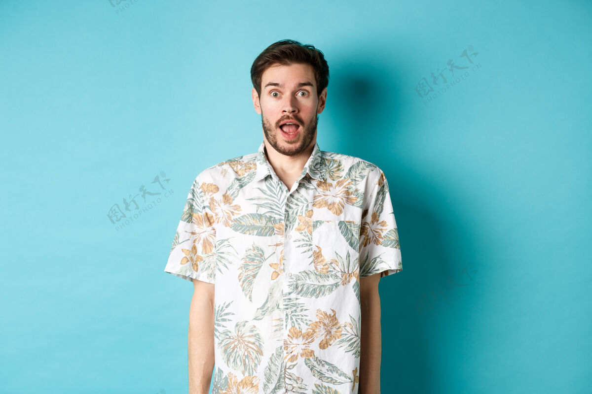 男人暑假一个穿着夏威夷衬衫的惊讶的家伙惊讶地喘息着 查看假期优惠 站在蓝色的背景上朋友帅哥肖像