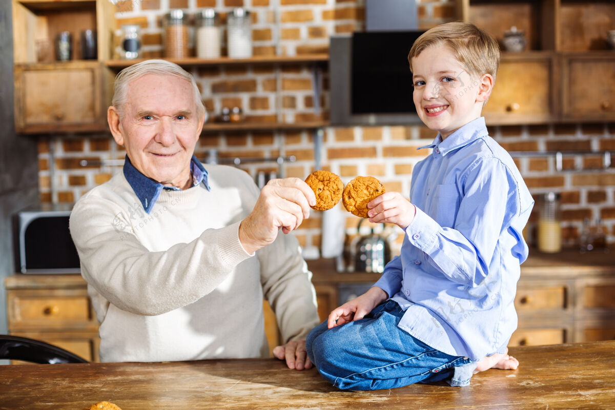 快乐快乐的小男孩坐在桌子上微笑着吃着自制的饼干烹饪甜点爷爷