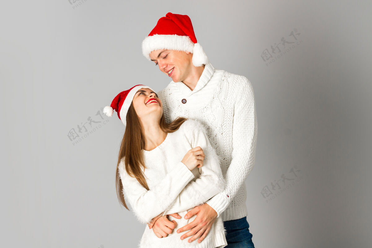 一年可爱的情侣在爱庆祝圣诞节 并在灰色墙上的工作室圣诞帽乐趣卡通情侣礼物