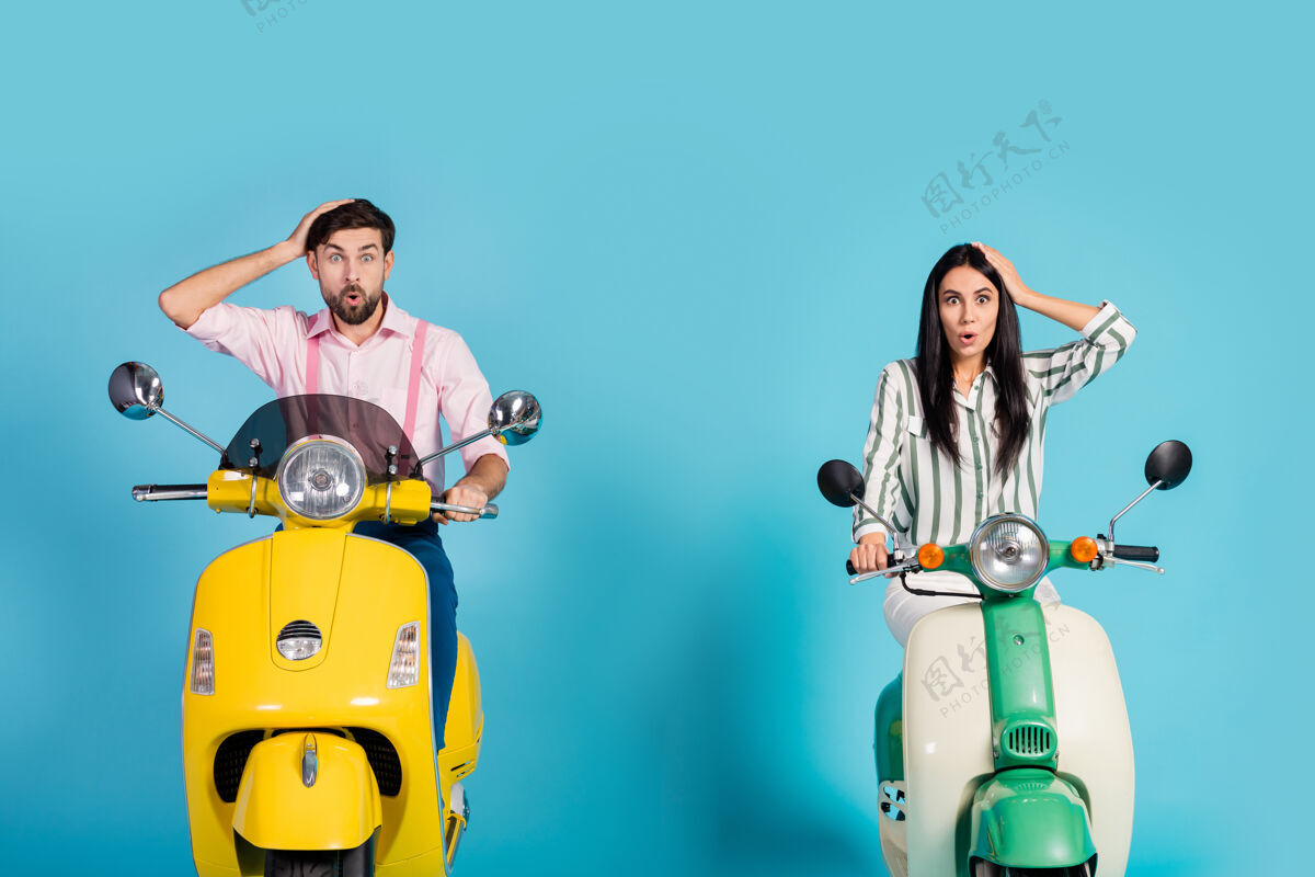 家庭惊讶的两个骑自行车的男人女人旅行黄绿色摩托车得到难以置信的想法 他们迷路了印象深刻的触摸手头尖叫哇天哪 隔着蓝色的墙摩托车男性一起