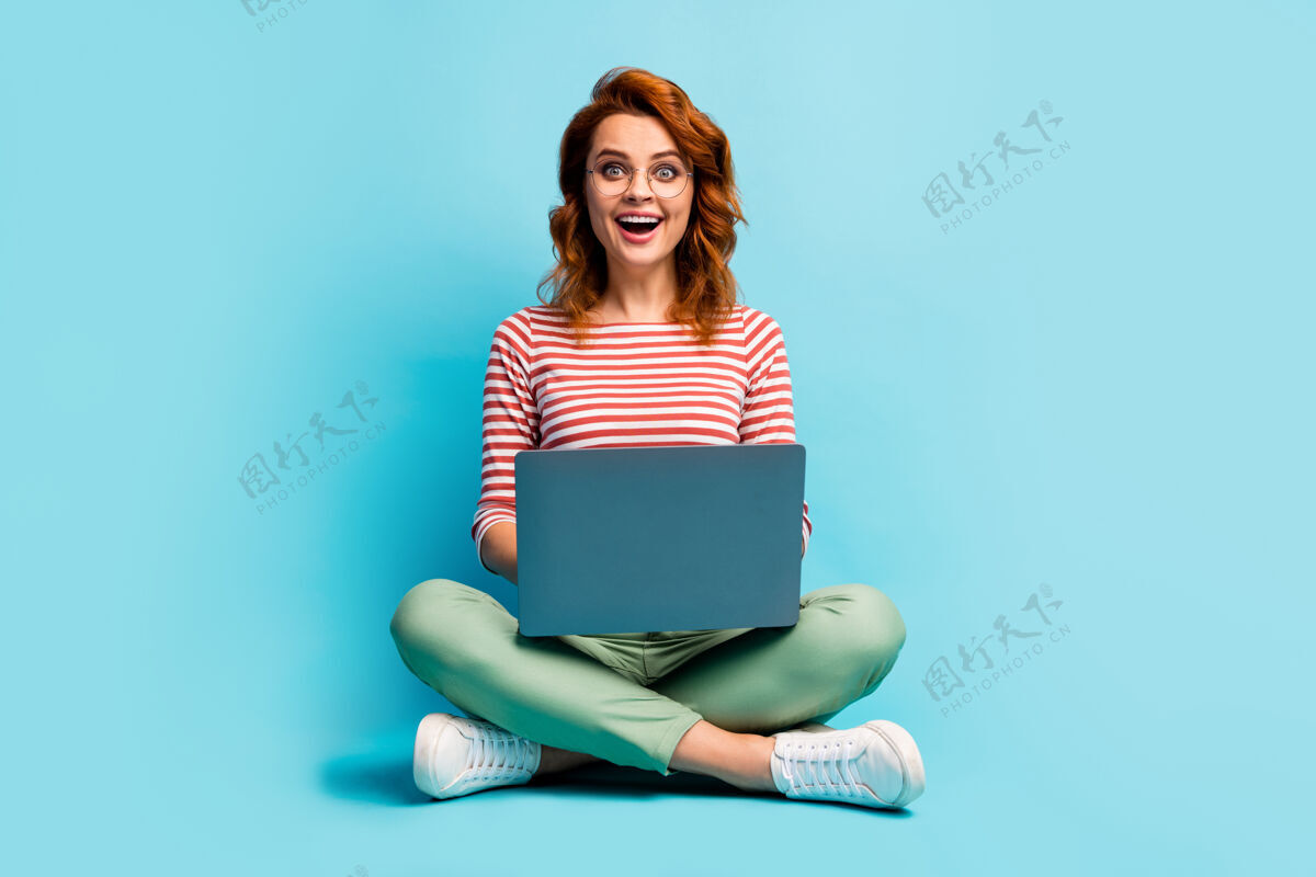 年轻全尺寸照片疯狂惊讶的女孩坐在地板上双腿交叉工作计算机搜索工作网站印象深刻尖叫哇omg穿时尚套装运动鞋隔离蓝色工作兴奋情感