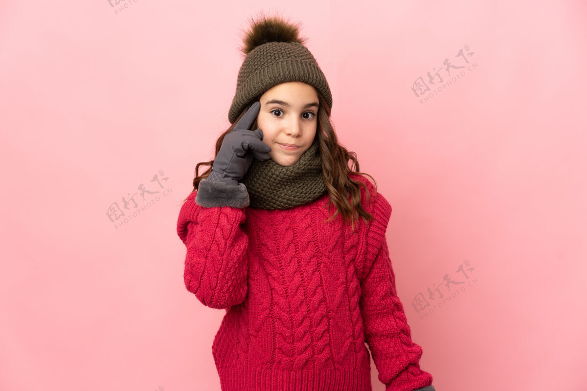聪明小女孩戴着冬天的帽子 孤零零地站在粉红色的墙上 想着一个主意寒冷戴思考