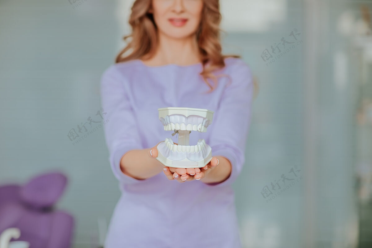 医疗年轻迷人的牙科医生的肖像 长卷发 身着紫色医疗制服 在橱柜里摆着塑料嘴正畸系统肖像