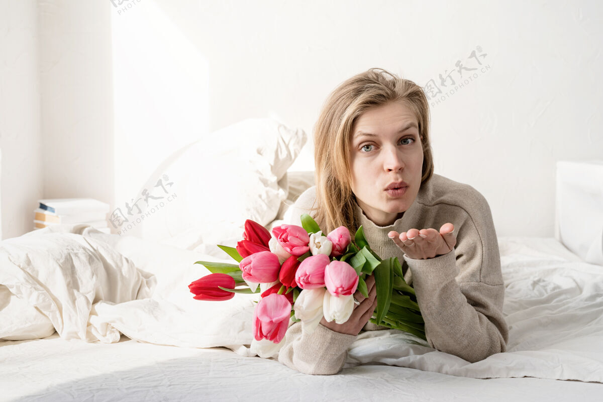爱情幸福的年轻女子穿着睡衣躺在床上捧着郁金香花束吹着吻浪漫房间美丽