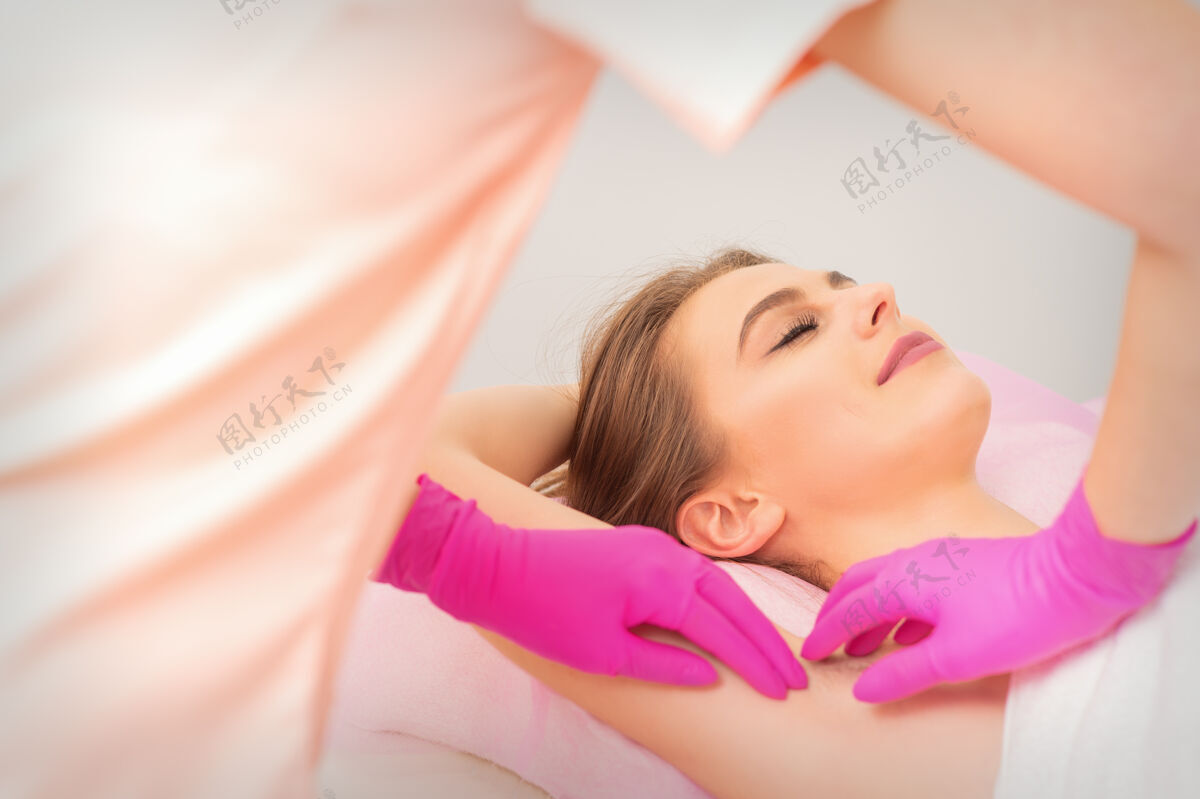 化妆品戴着手套手拿腋窝打蜡的女人身体护理皮肤
