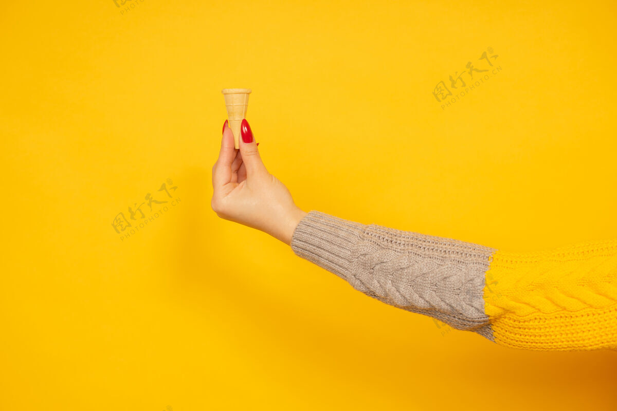 花式女人手里拿着黄色背景上孤立的小空脆冰淇淋筒毛衣吃香草