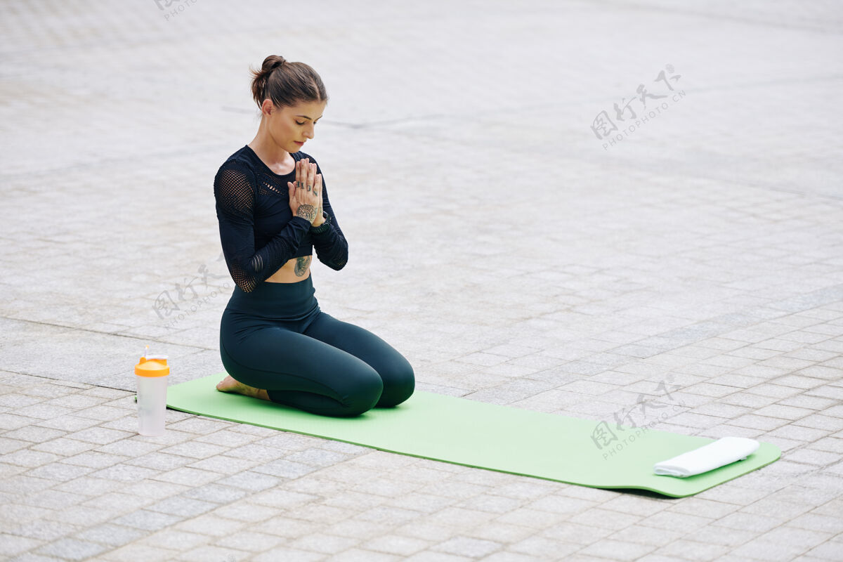 运动适合在户外瑜伽垫上冥想的年轻女性她闭着眼睛坐着 双手握在手心里活动休闲活动冥想
