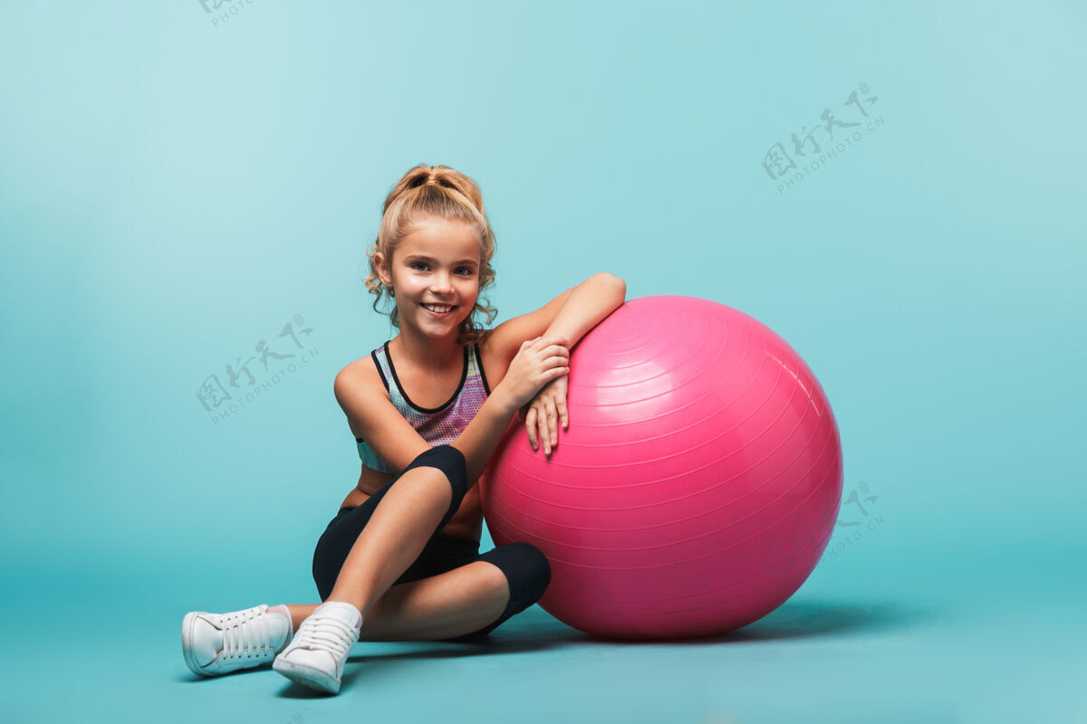 童年快乐的小女孩穿着运动服 靠在一个健身球上 隔着蓝色的墙运动玩耍快乐