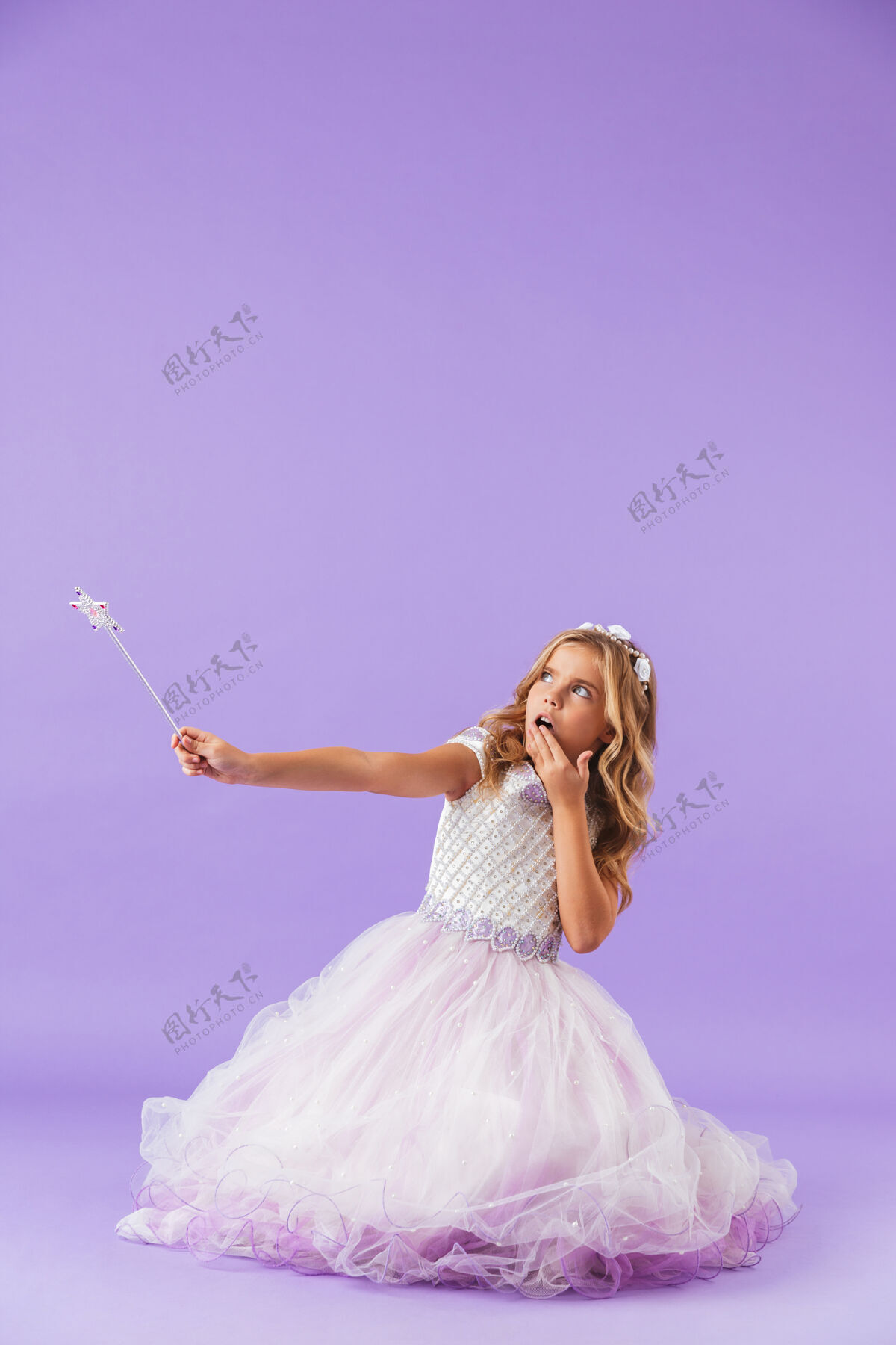 庆祝穿着公主裙的漂亮小女孩孤零零地坐在紫罗兰色的墙上 手里拿着魔杖欢乐美丽五颜六色