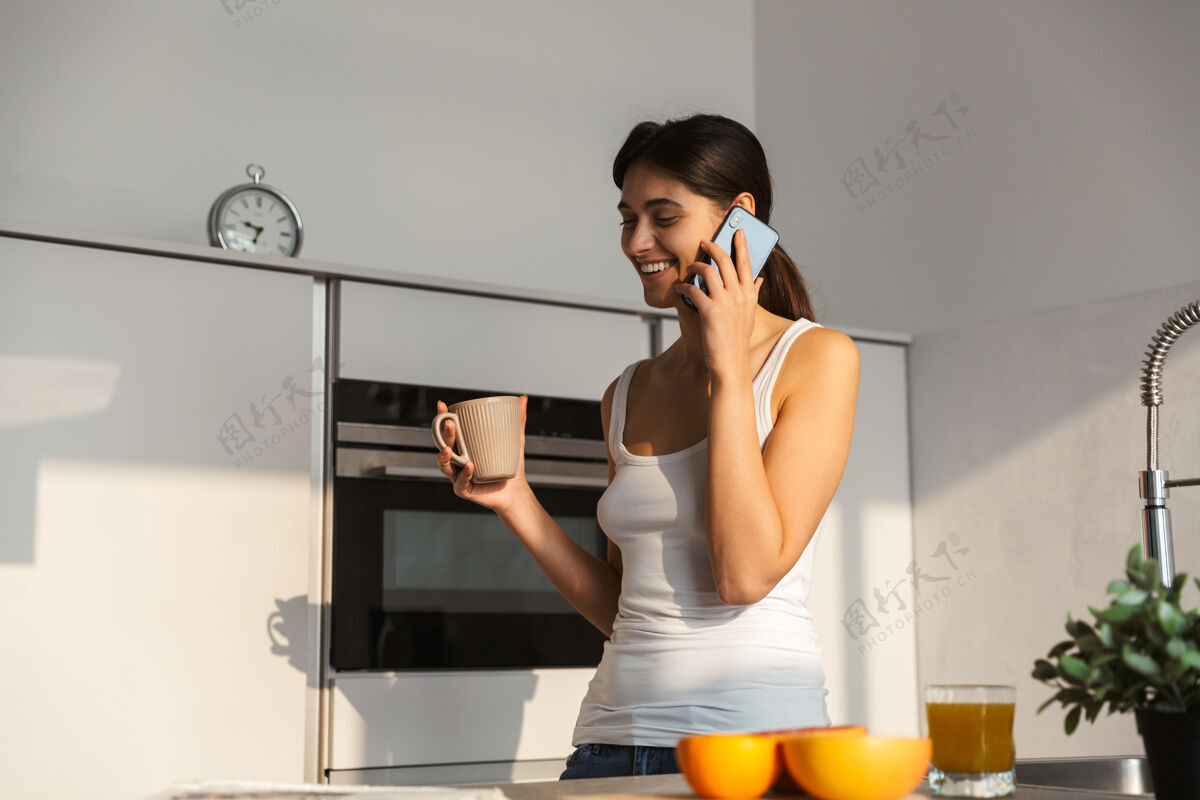 长相早上站在厨房里喝着咖啡 讲着手机的漂亮女孩茶年轻肖像
