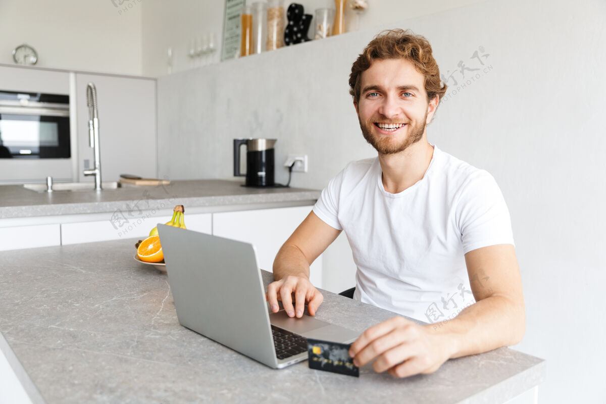 吸引快乐的小胡子男人在家里的桌子旁用手提电脑拿着信用卡聊天柔软男人教育