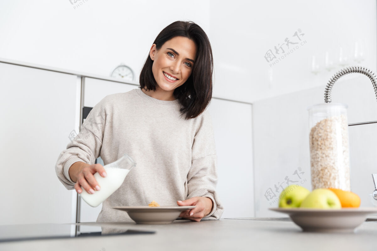 景点30多岁的美女站在家里的现代厨房里 一边用燕麦片和水果做早餐成人可爱舒适