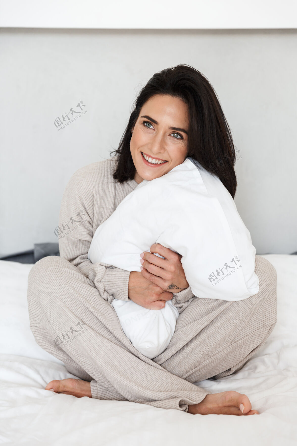 满足30多岁的美女坐在床上 枕着白色的枕头 在家休息成熟深色头发舒适