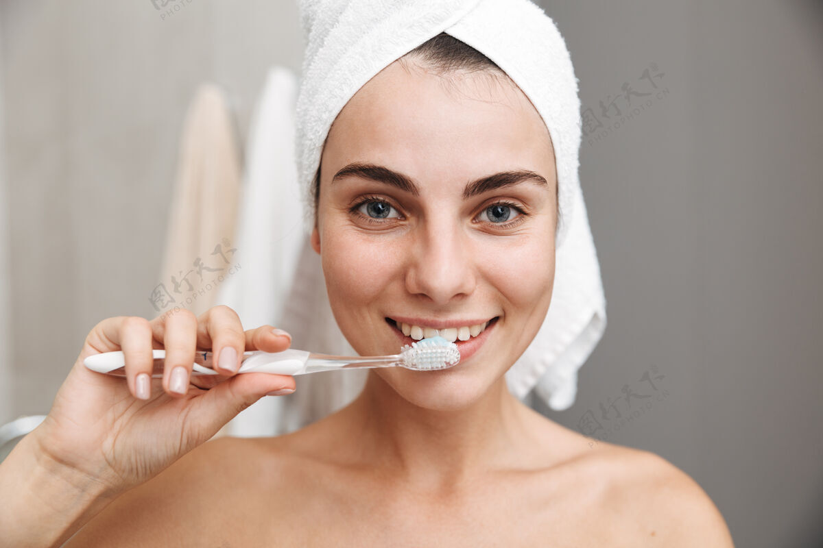 牙膏特写镜头：一个头上戴着毛巾的漂亮年轻女子站在浴室里刷牙白种人漂亮牙刷