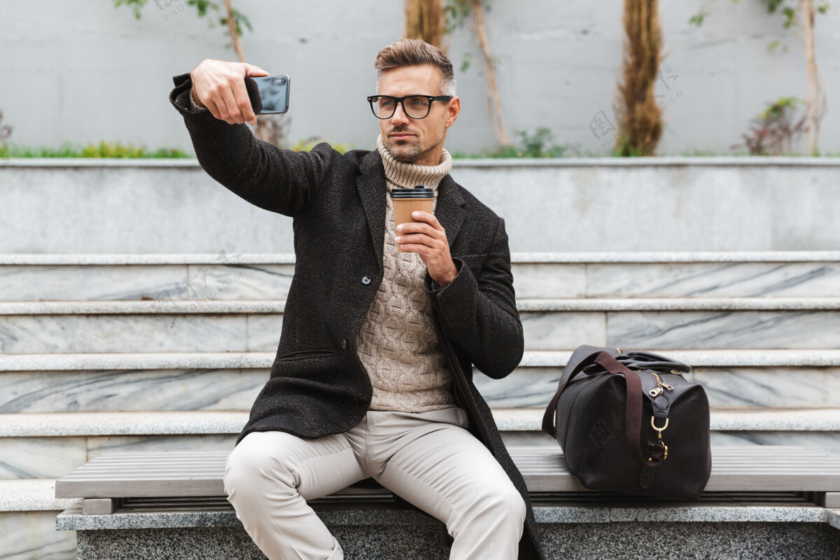 毛衣穿着夹克的帅哥坐在户外自拍 手里拿着一杯外卖咖啡杯子肖像Wifi