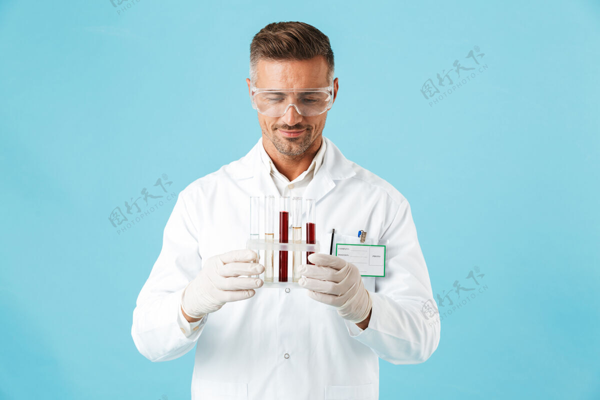 医院一位英俊的成熟男子医生在蓝色的墙上举着带血的试管摆姿势中年治疗医疗
