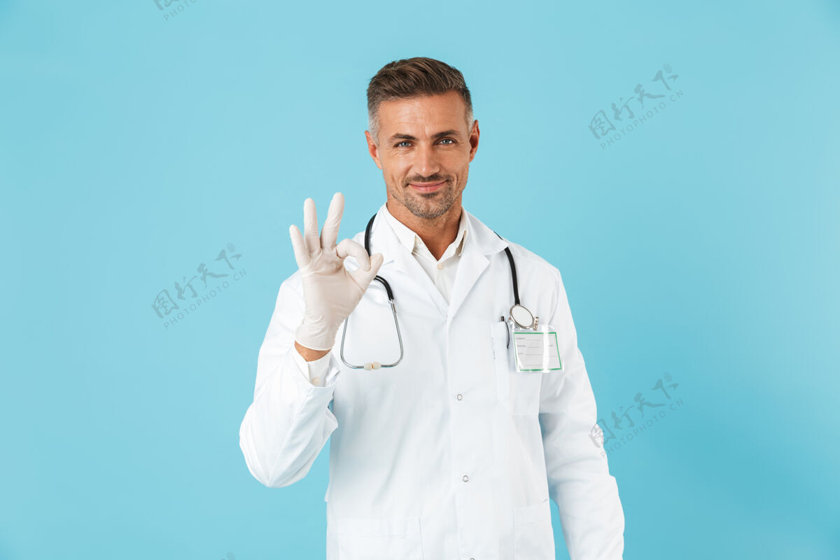 制服一个英俊的成熟男子医生在蓝色的墙上摆姿势 显示出良好的姿态孤立的照片情绪听诊器专家