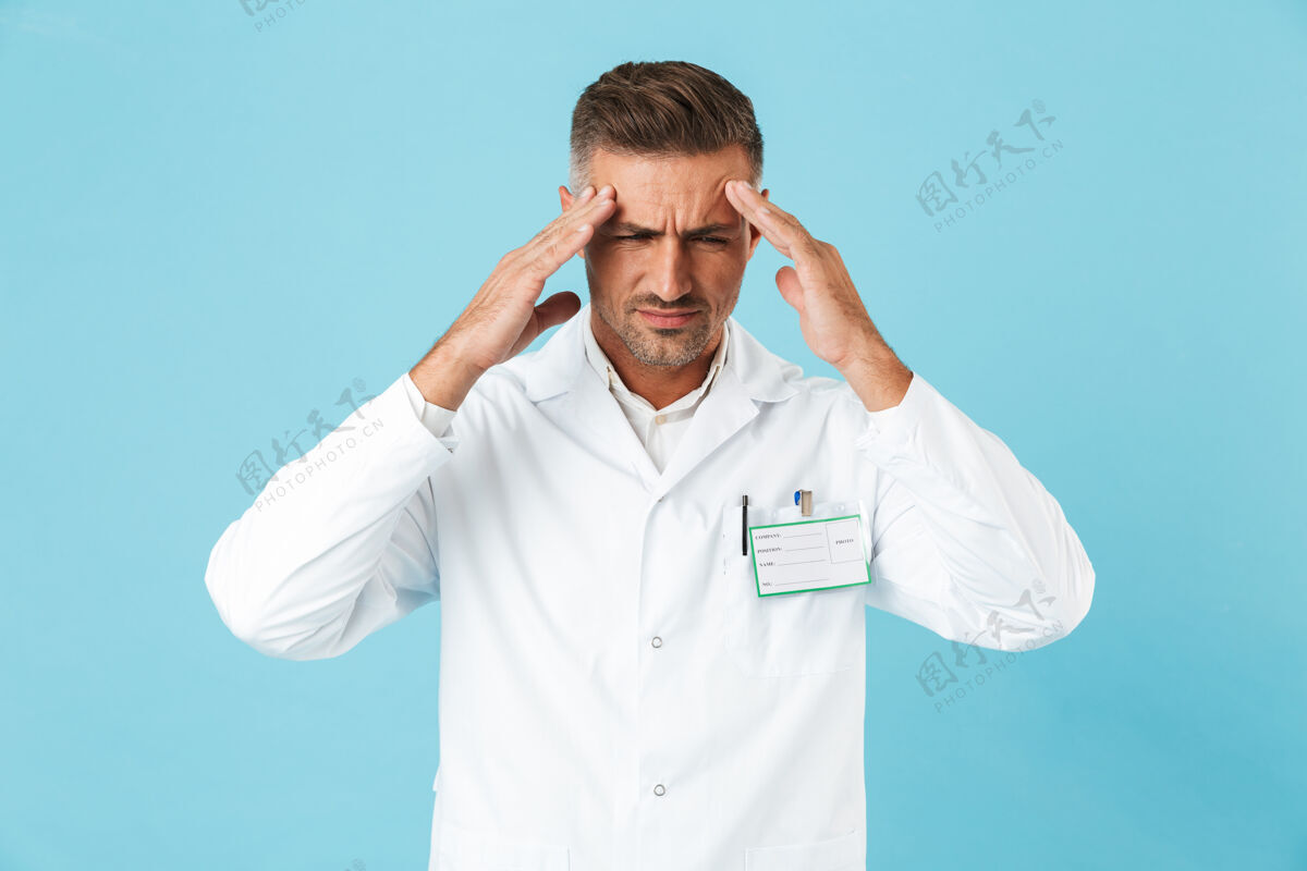 沮丧疲倦的男人医生穿着制服孤立地站在蓝色的墙上 头痛疲倦医生压力