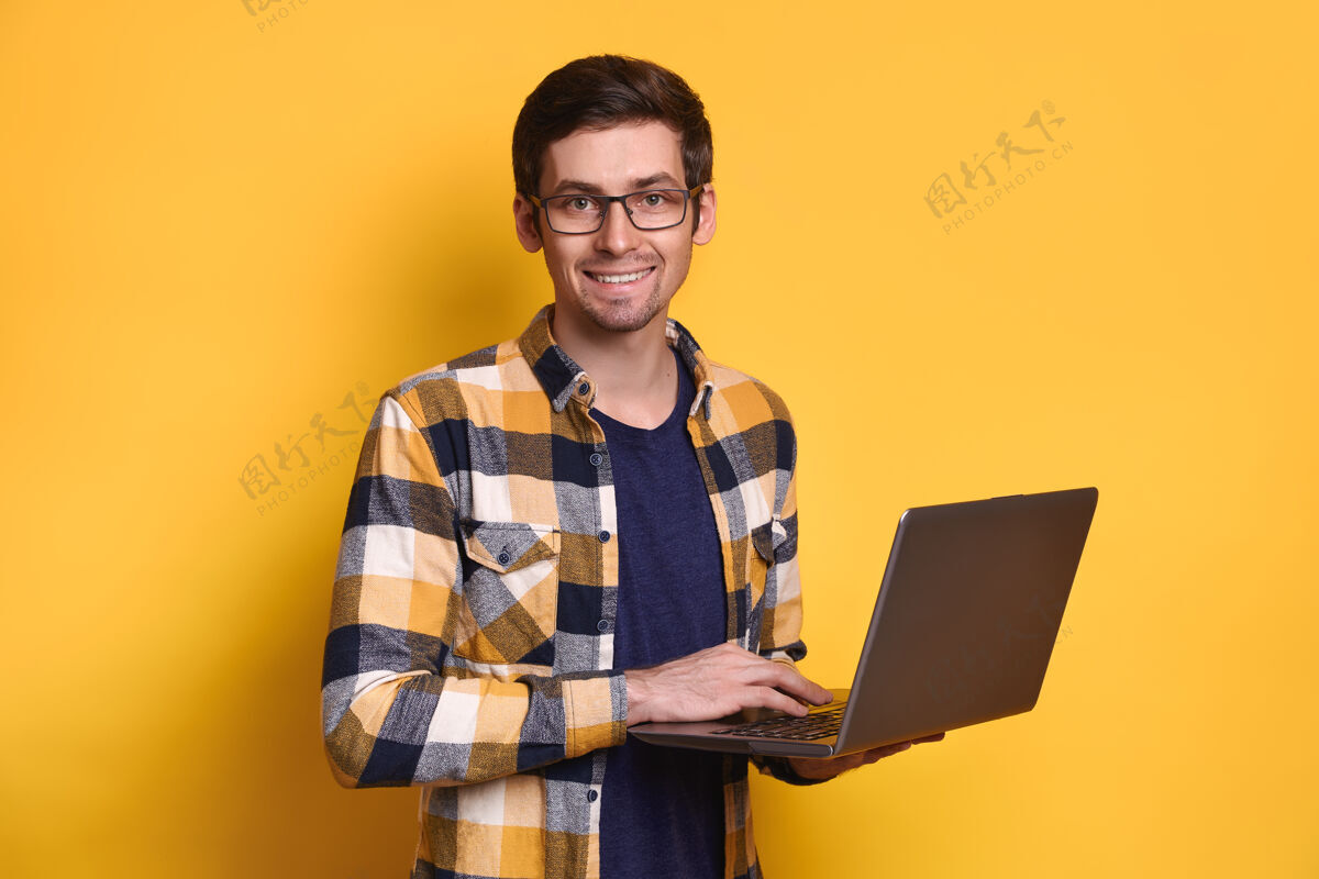 商务人士戴眼镜的年轻帅气的黑发男人正幸福地微笑着 手里拿着黄色的笔记本电脑教育通信笔记本电脑