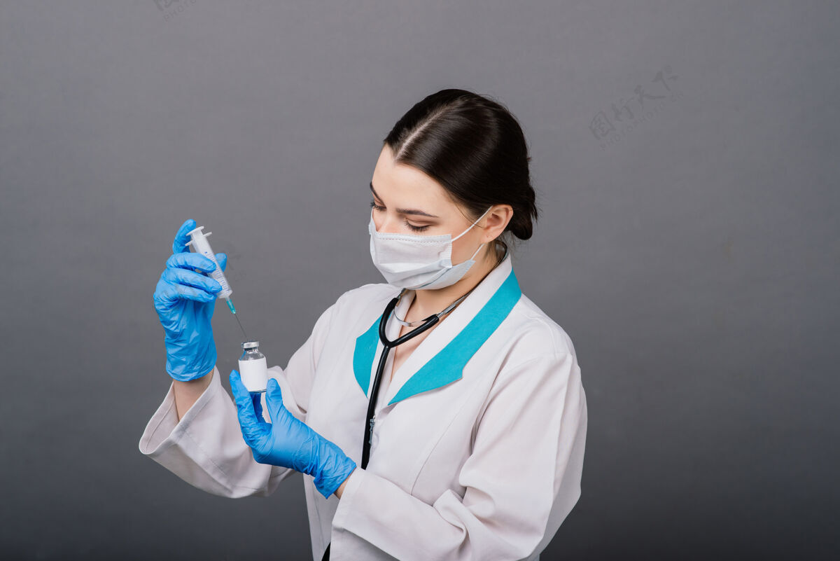 专业人员严肃的女医生戴着医用口罩拿着注射器和疫苗隔离在灰色上白人年轻人医疗保健