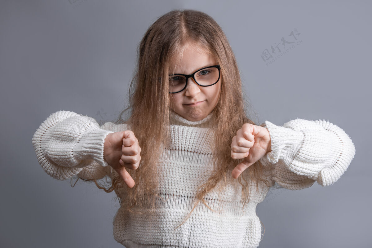 向下一个年轻漂亮的金发小女孩的肖像 穿着毛衣 不满意的怀疑者竖起大拇指表示不喜欢负面恨随意