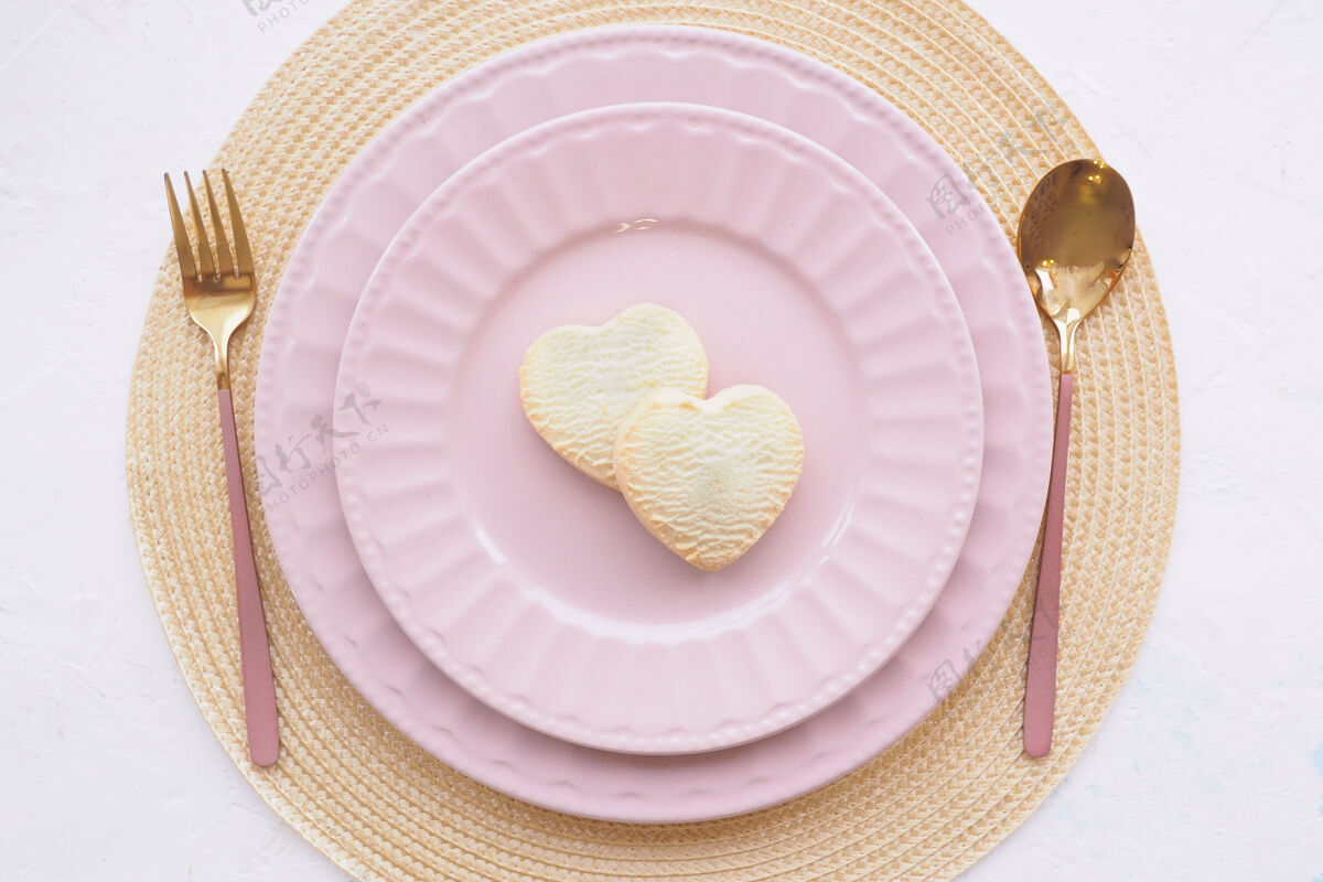 浪漫表格设置两个空的粉红色盘子 两个心形饼干 一把勺子和一把叉子放在一张白色的桌子上叉子盘子勺子