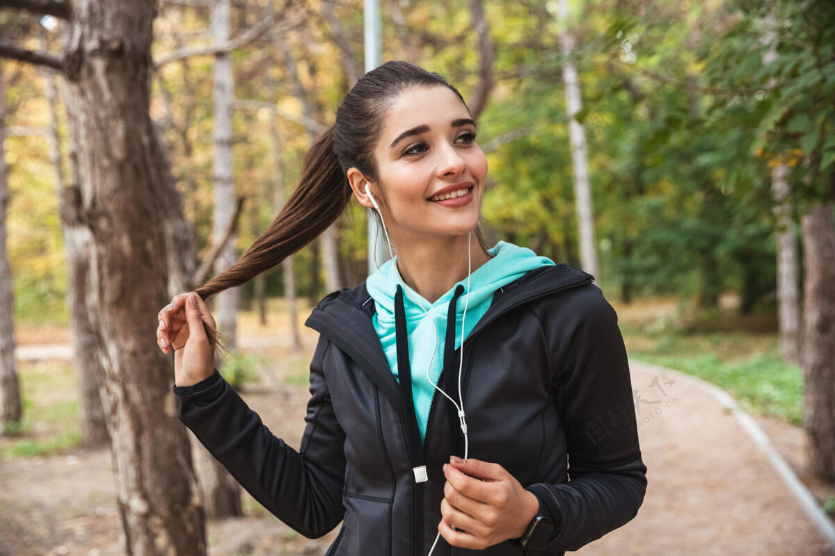 生活方式微笑的健身女 戴着耳机听音乐 手持手机站在公园里成人音乐公园