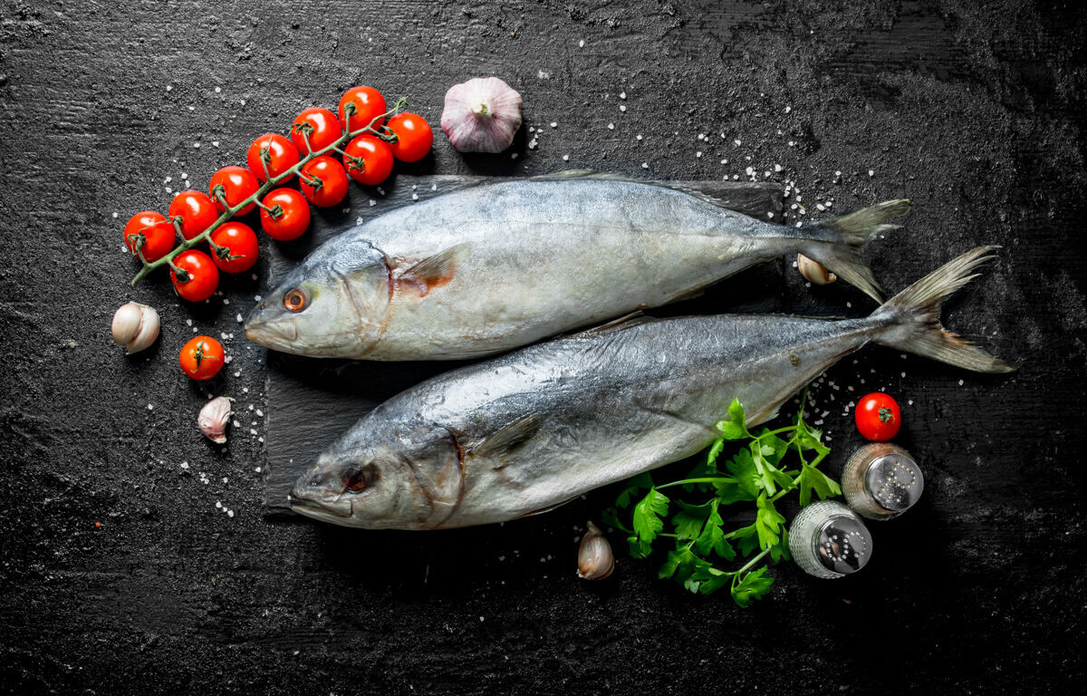 海洋生鱼金枪鱼配樱桃番茄和蒜瓣放在黑色乡村餐桌上美味渔获物健康