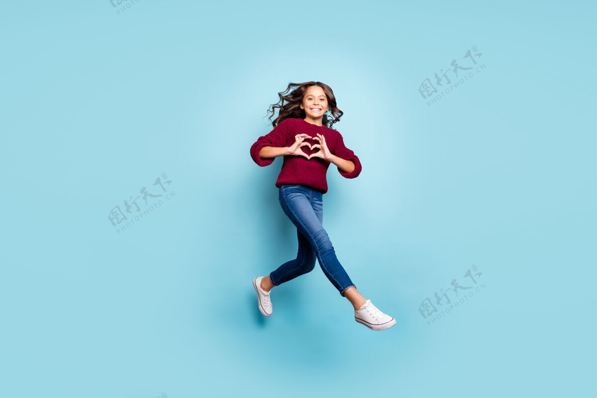 浪漫开朗正面女友跳楼跑步展示心形标志穿牛仔裤牛仔紫红色毛衣孤立蓝色生动色彩背景的全身照片休闲空气表演