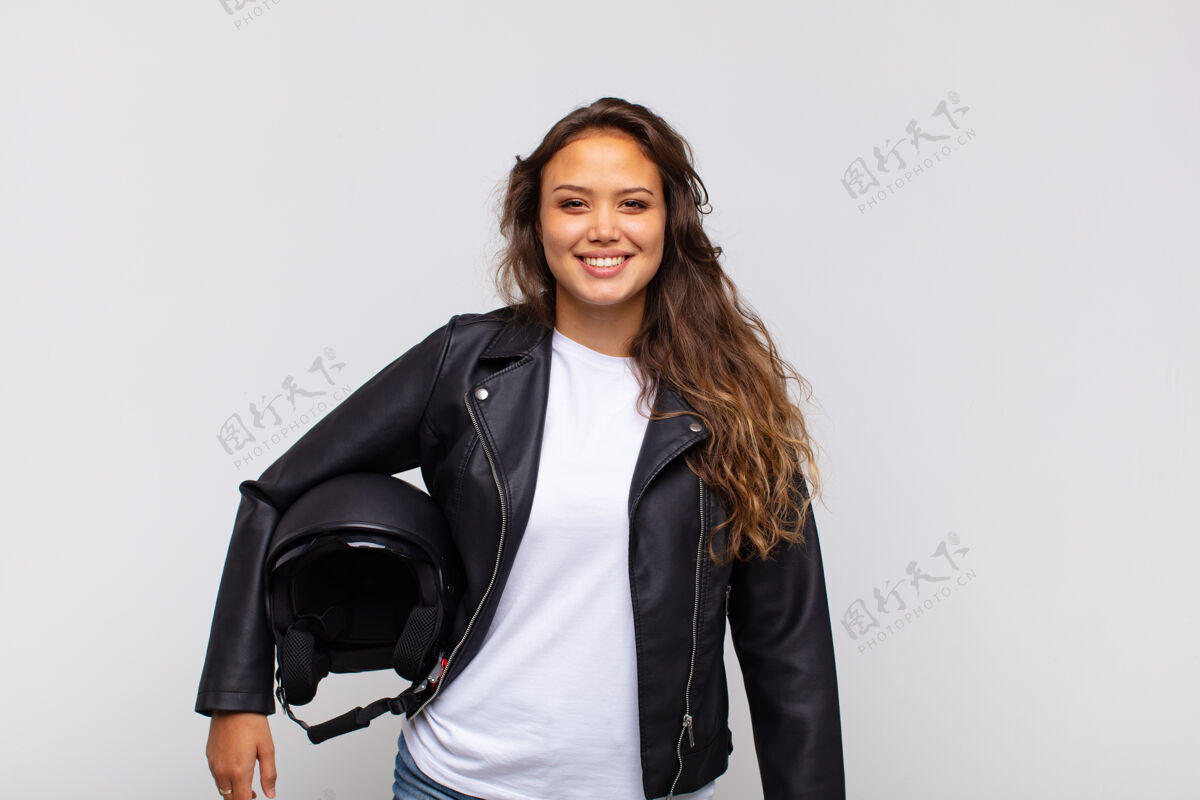 骑手年轻的女摩托车手微笑着 手放在臀部 自信 积极 自豪和友好的态度皮革赛车满意